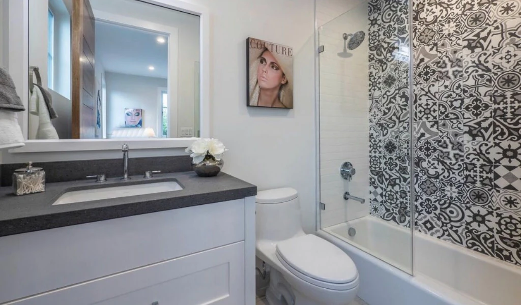 Modern bathroom with patterned shower tiles, silver fixtures, and a decorative mirror over the sink.