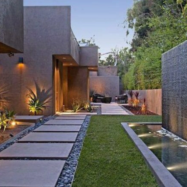 Modern garden pathway with stepping stones, a narrow water feature, and lush greenery alongside geometric architecture.