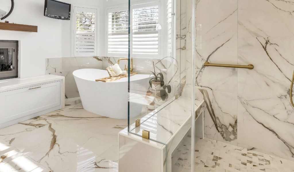 Modern bathroom with marble tiles featuring a freestanding tub, glass shower enclosure, and white vanity.