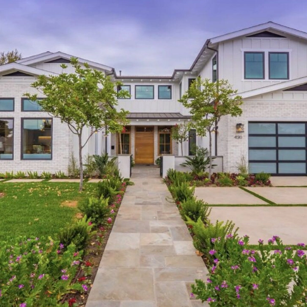 The exterior of a sleek black and white modern home after a remodel. Green grass and trees line the pathway to the front entrance.