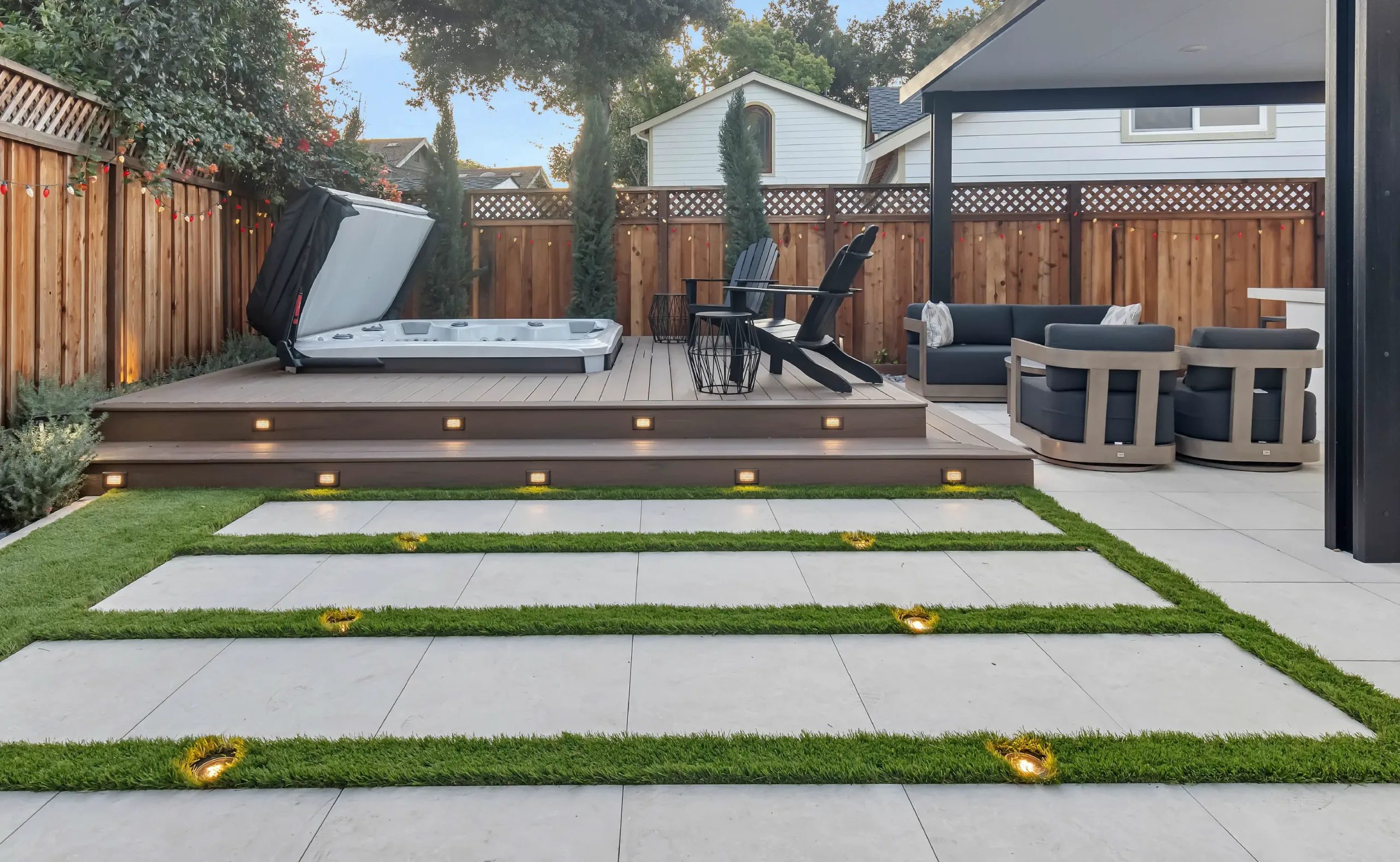 Modern backyard with hardscaping design featuring large concrete pavers, artificial turf inlays, deck lighting, spa area, and outdoor seating with privacy fencing—perfect inspiration for a luxury backyard remodel.