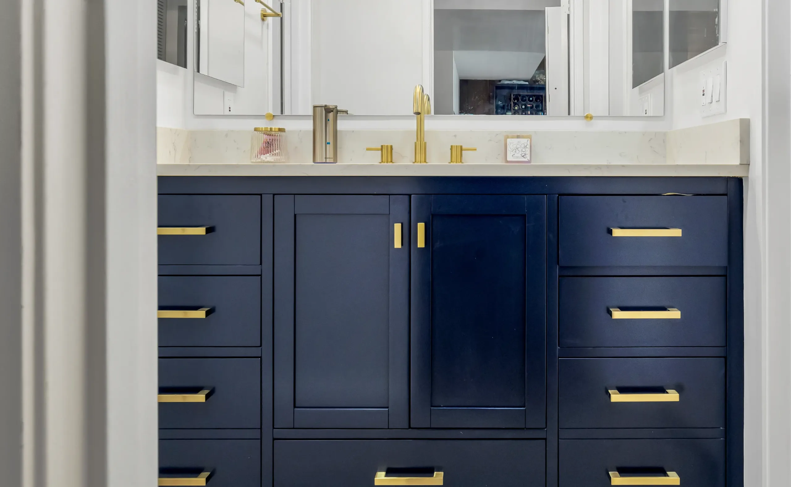 Modern bathroom vanity with deep navy blue cabinets, gold hardware, and a white quartz countertop with gold faucet fixtures.