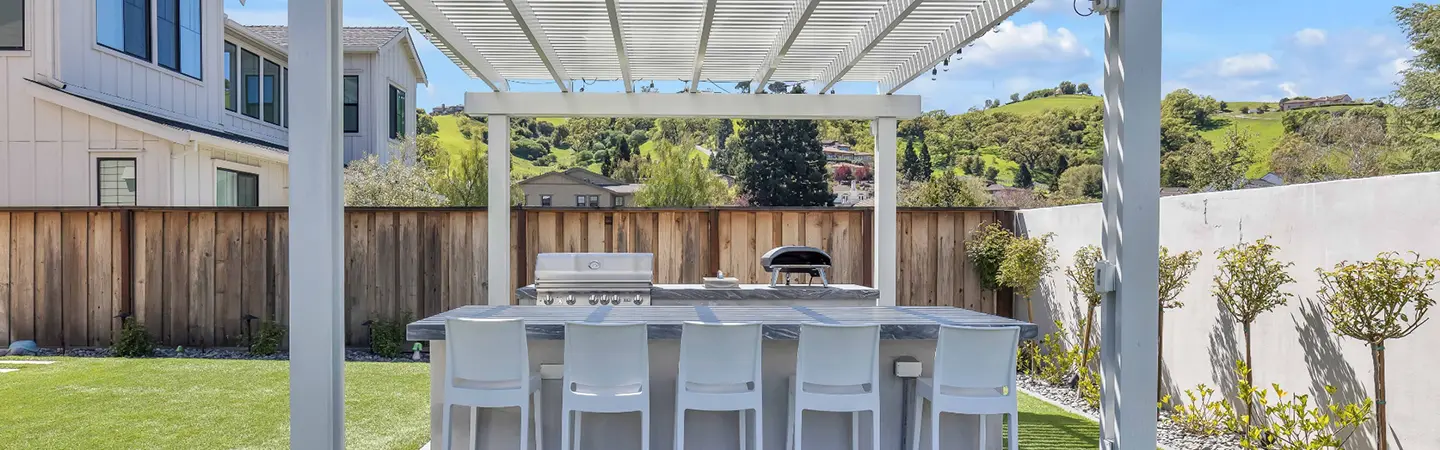 An outdoor living space with a pergola, bar stools, and a grill, showcasing Asher Brothers Construction's pergolas and patio covers.