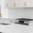 A kitchen detail with white cabinets, a large black island, and gold hardware above the waterfall granite island.