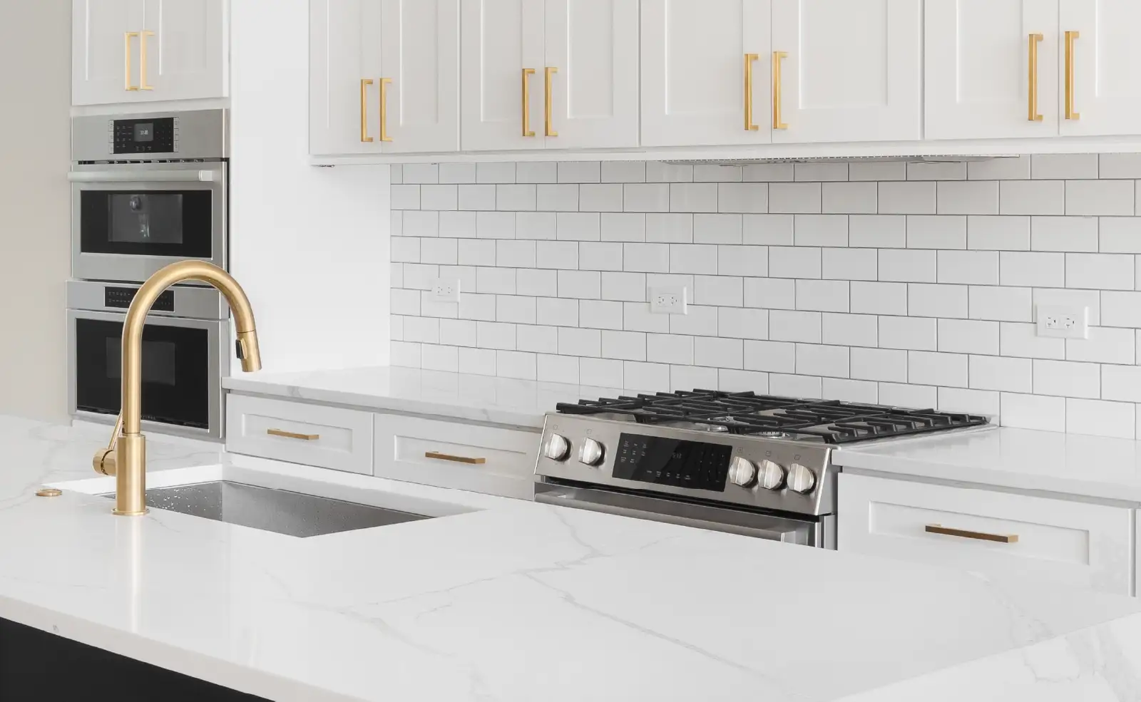 A kitchen detail with white cabinets, a large black island, and gold hardware above the waterfall granite island.